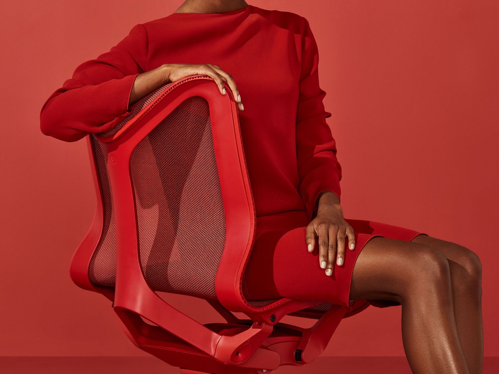 Uma mulher em um vestido vermelho senta-se em uma cadeira Cosm lombar em vermelho Canyon.